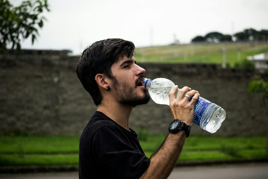 ULTIMATE FITNESS GUIDE FOR MEN AND BOYS: BUILD STRENGTH, eNERGY & CONFIDENCE NATURALLY A young man drinks bottled water outside, staying hydrated and refreshed.